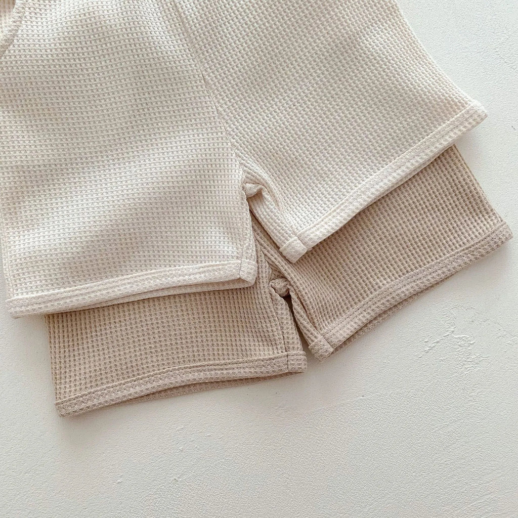 Unisex baby summer suit with bear print cotton top and beige shorts on a neutral background