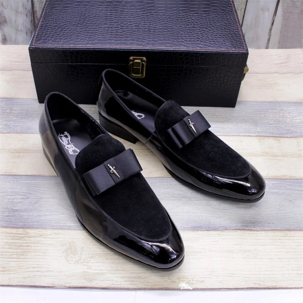Men's glossy black patent leather tassel loafers with a low-top design and rubber sole on a wooden floor.