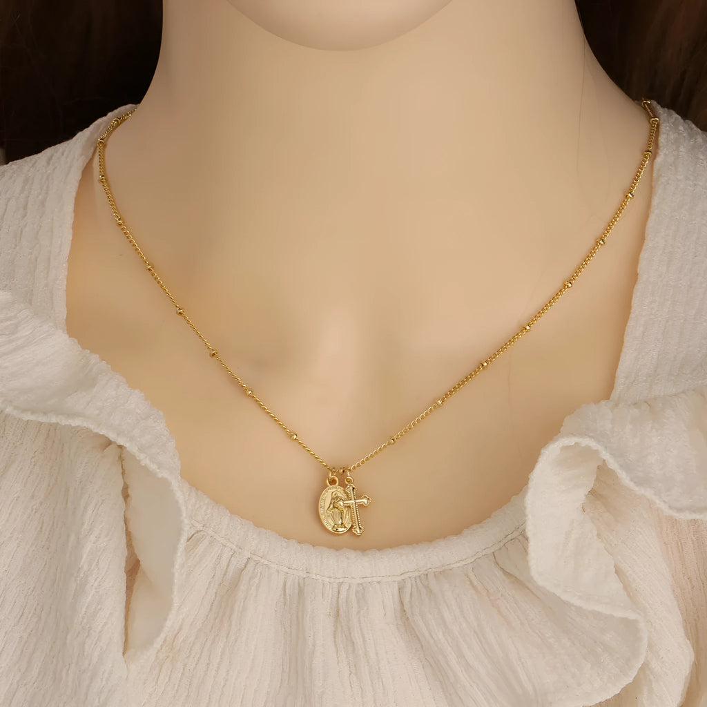 Geometric gold cross Virgin Mary pendant necklace with a simple design on a chain.