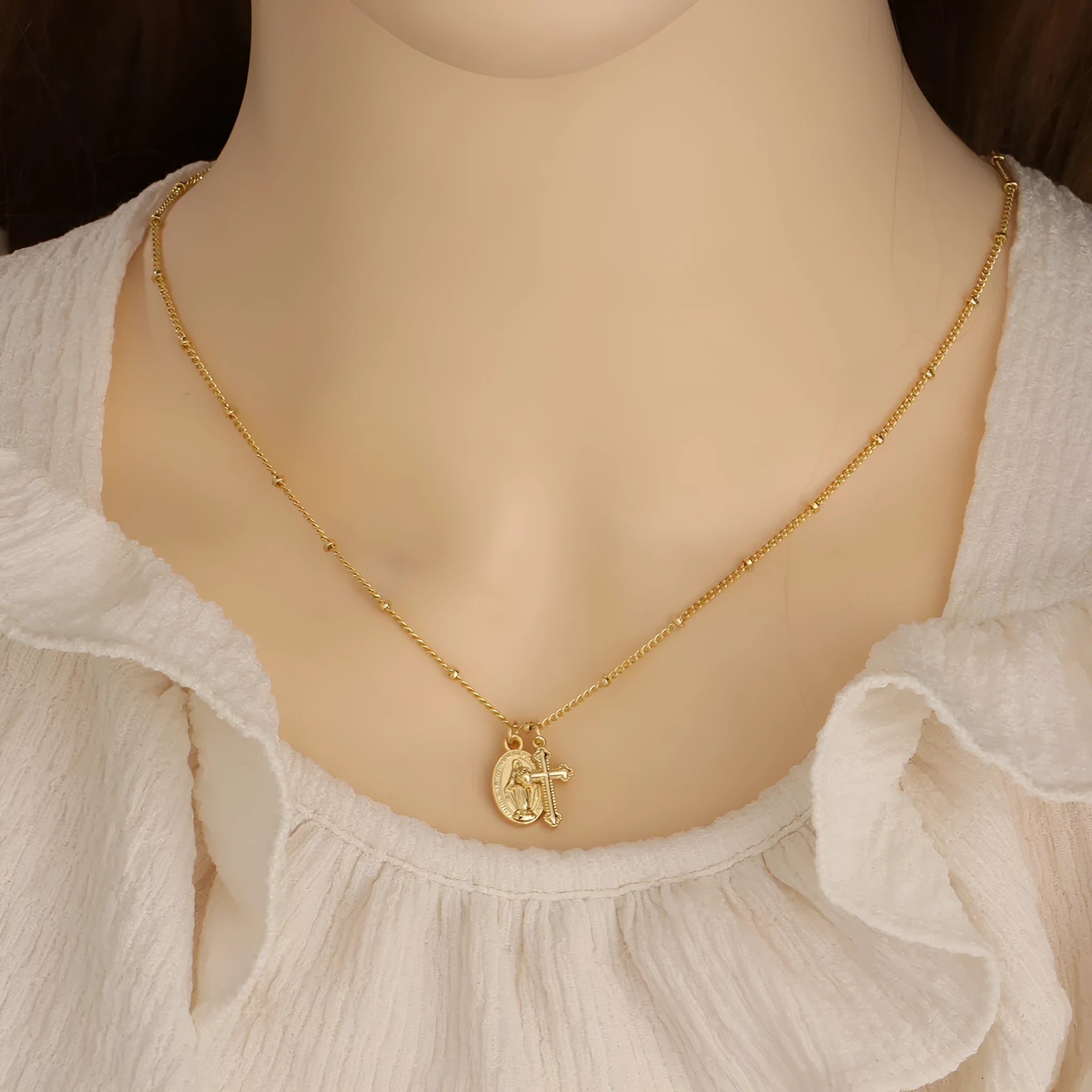 Geometric gold cross Virgin Mary pendant necklace with a simple design on a chain.