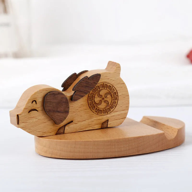 Solid beech wood phone stand with a decorative resin puppy figurine, holding a mobile phone at an angle with a charging cable threaded through the back.