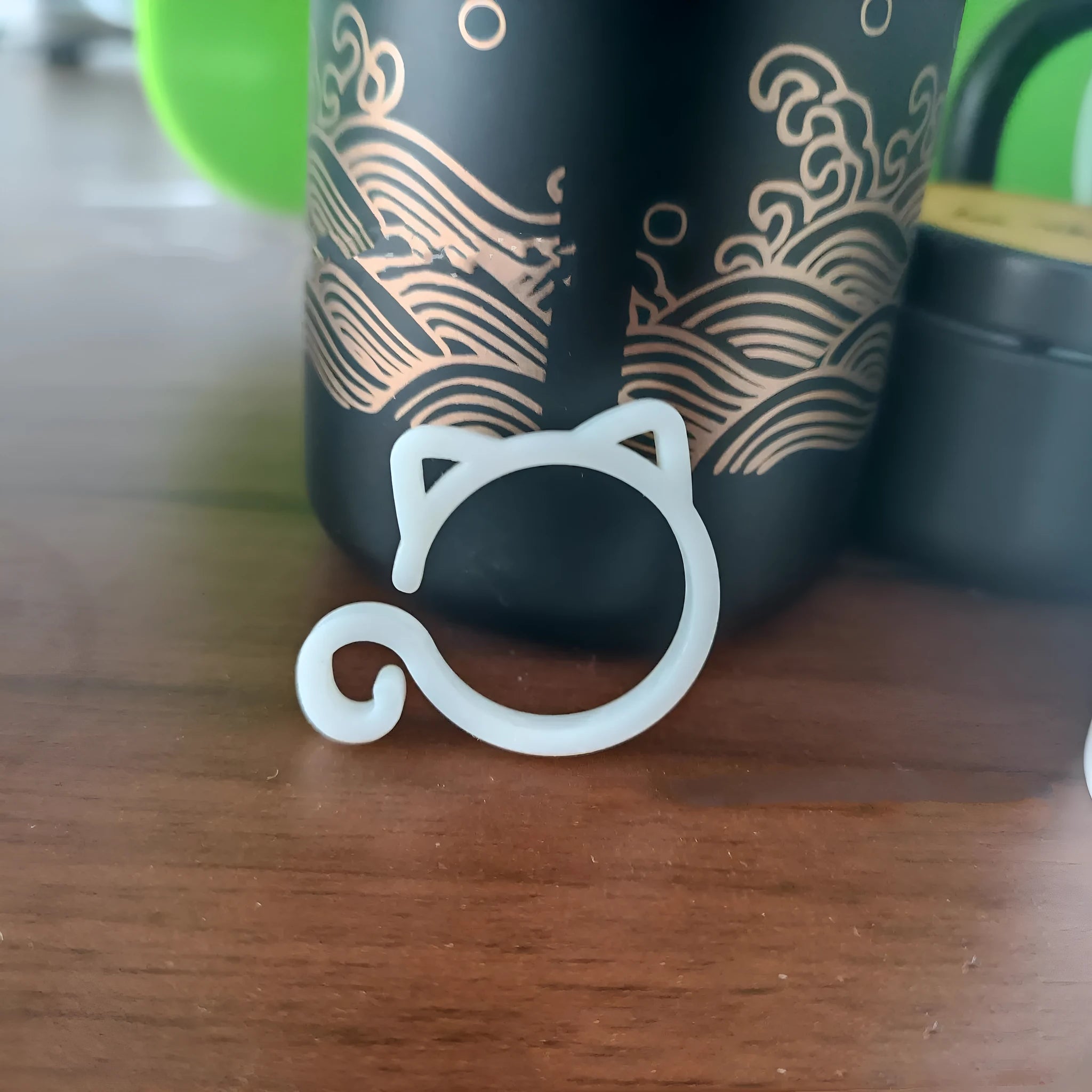A small red cat-shaped plastic clip for holding plant stems, shown next to a green leaf.