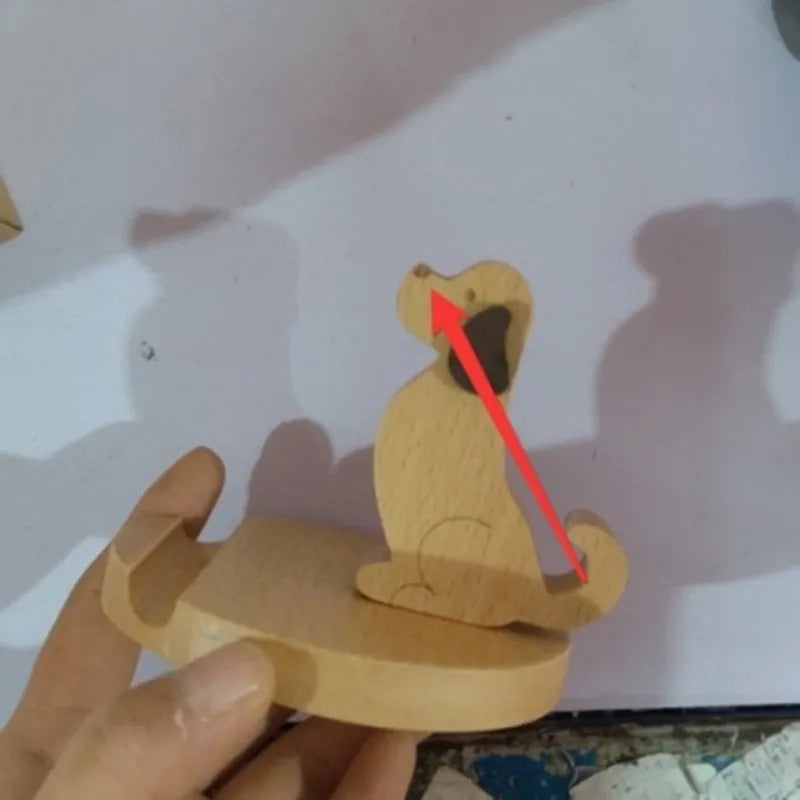 Solid beech wood phone stand with a decorative resin puppy figurine, holding a mobile phone at an angle with a charging cable threaded through the back.