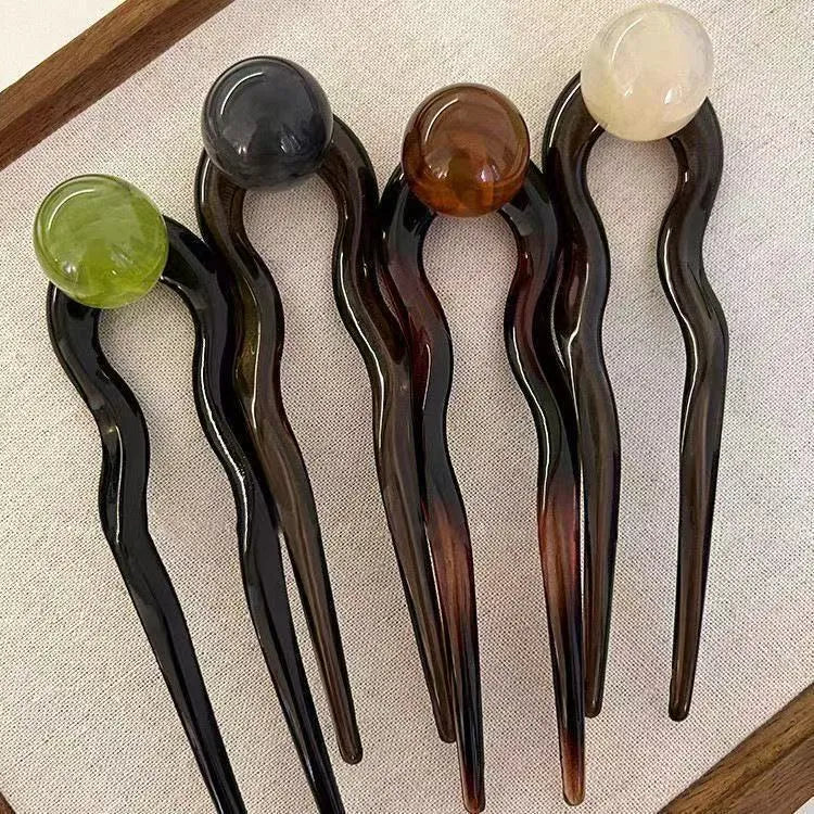 A set of U-shaped acrylic hair barrettes with a ball detail in beige, caramel, dark grey, and green colours