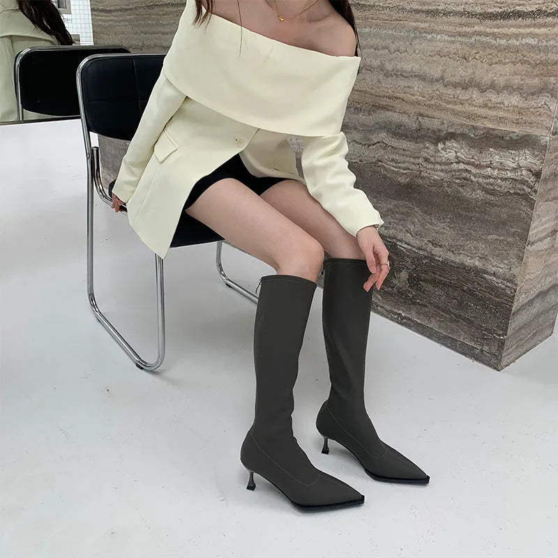 Women's black pointed toe below-knee boots with a stiletto heel and a back zipper on a plain background.