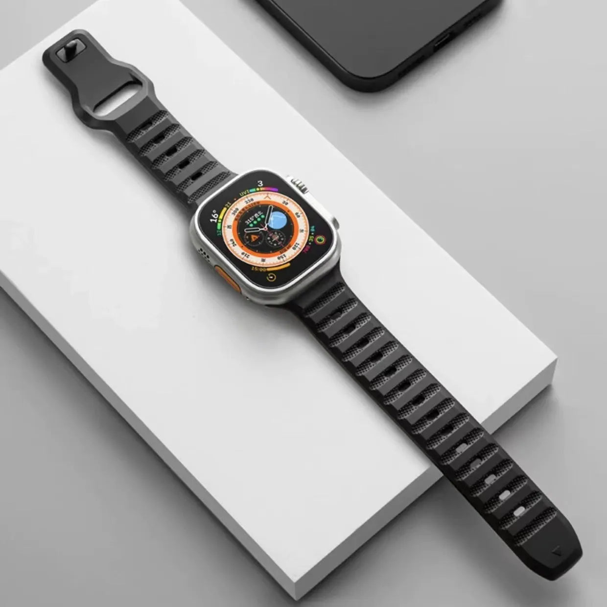 Black fluoro rubber Apple Watch strap with T-buckle closure shown detached from watch.