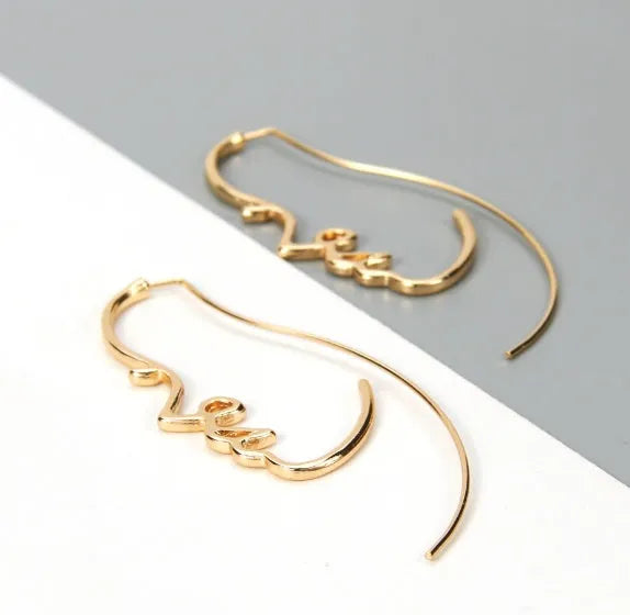 Creative abstract face contour earrings in metal gold finish on a white background