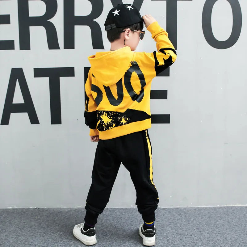 A boy wearing a black Korean-style hooded cotton tracksuit set with a letter print, featuring long sleeves and matching trousers.