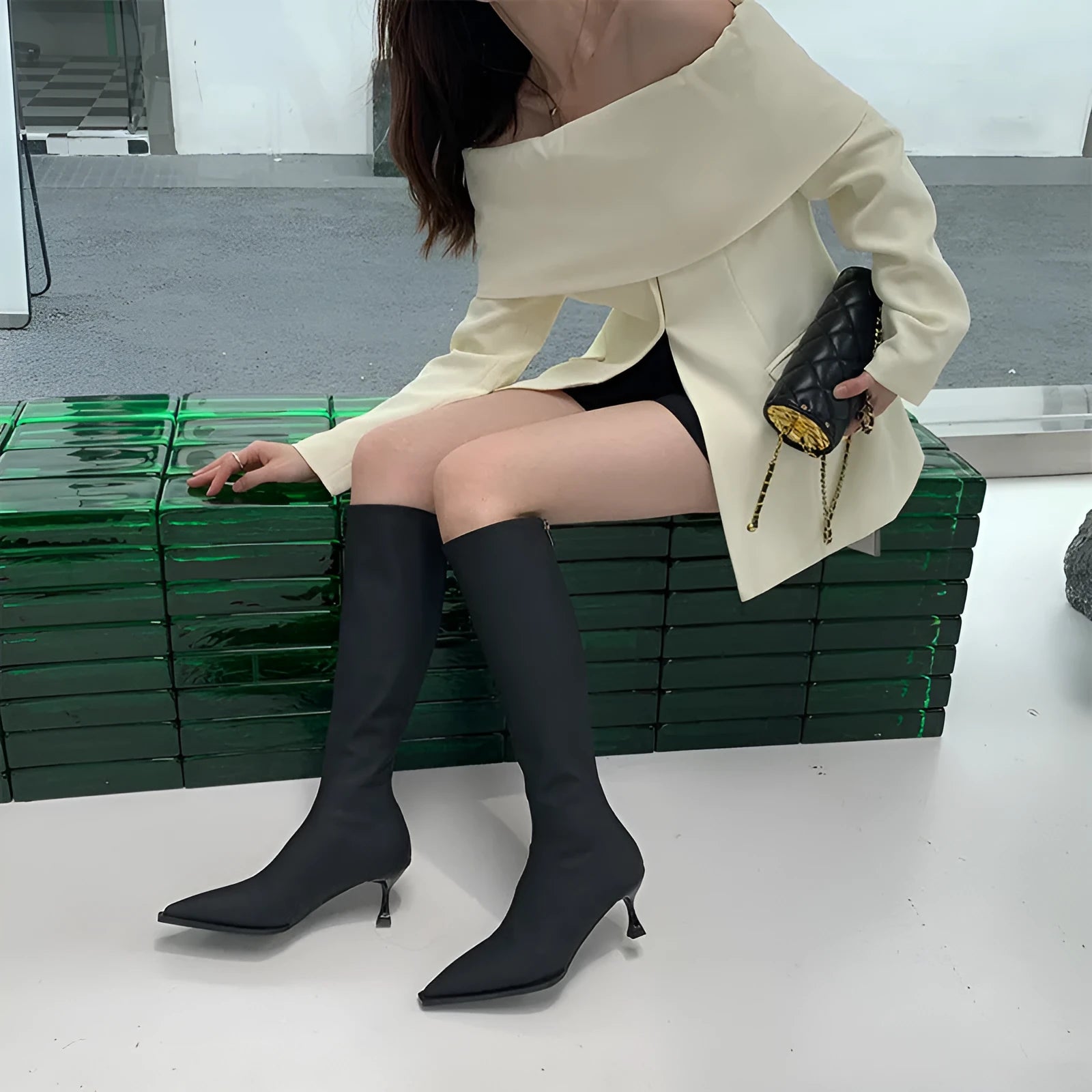Women's black pointed toe below-knee boots with a stiletto heel and a back zipper on a plain background.