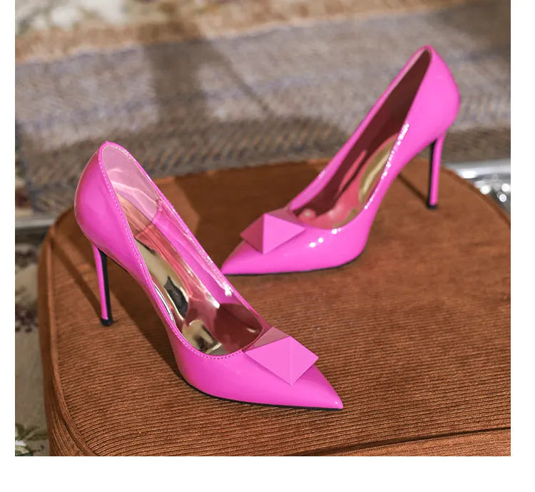 Pink patent leather women's stiletto heels with pointed toe, buckle strap, and rivet detail on a shallow cut.