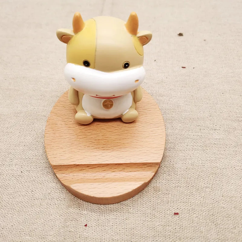 Solid beech wood phone stand with a decorative resin puppy figurine, holding a mobile phone at an angle with a charging cable threaded through the back.