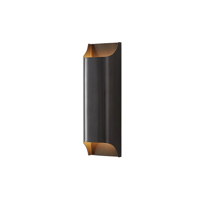 Minimalist copper wall lamp in black gold finish mounted beside a bed.