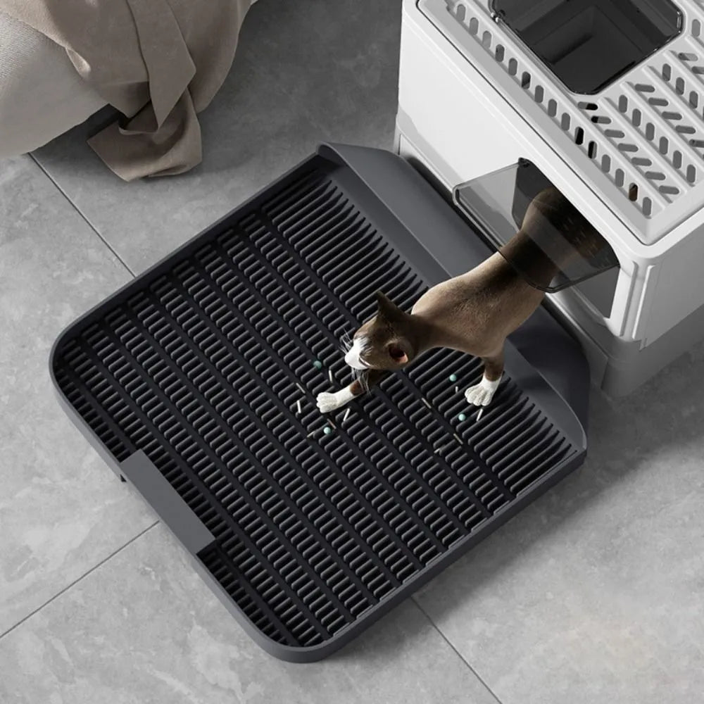 Large black cat litter pedal mat with slanted design next to a litter box.