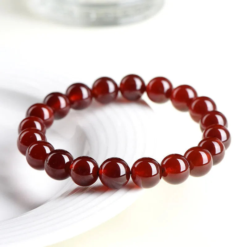 Close-up of a natural orange red garnet bead bracelet with a metal Ruyi charm on a wrist.