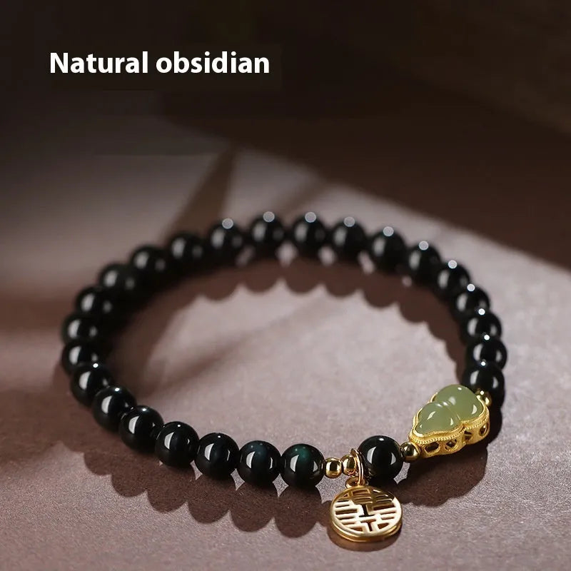 Black obsidian bracelet with a carved Hetian jade gourd charm, showing geometric beads.
