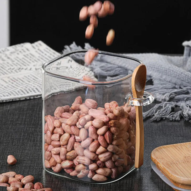 Square glass storage jar for coffee beans with wooden spoon on kitchen counter, clear body shows contents