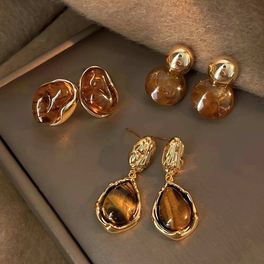 Handmade geometric alloy earring set showing three styles: round pieces, amber studs, and tigereye drops with tassels.