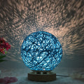 Rattan ball table lamp with woven shade and warm LED lighting on wooden surface