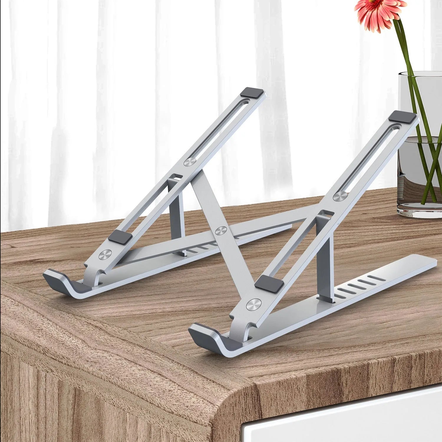 Silver aluminum folding laptop stand shown at an angle on a desk