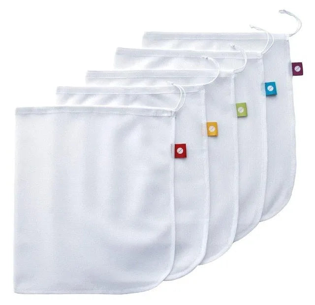 Five white cotton drawstring bags for kitchen vegetable storage arranged on a clean surface