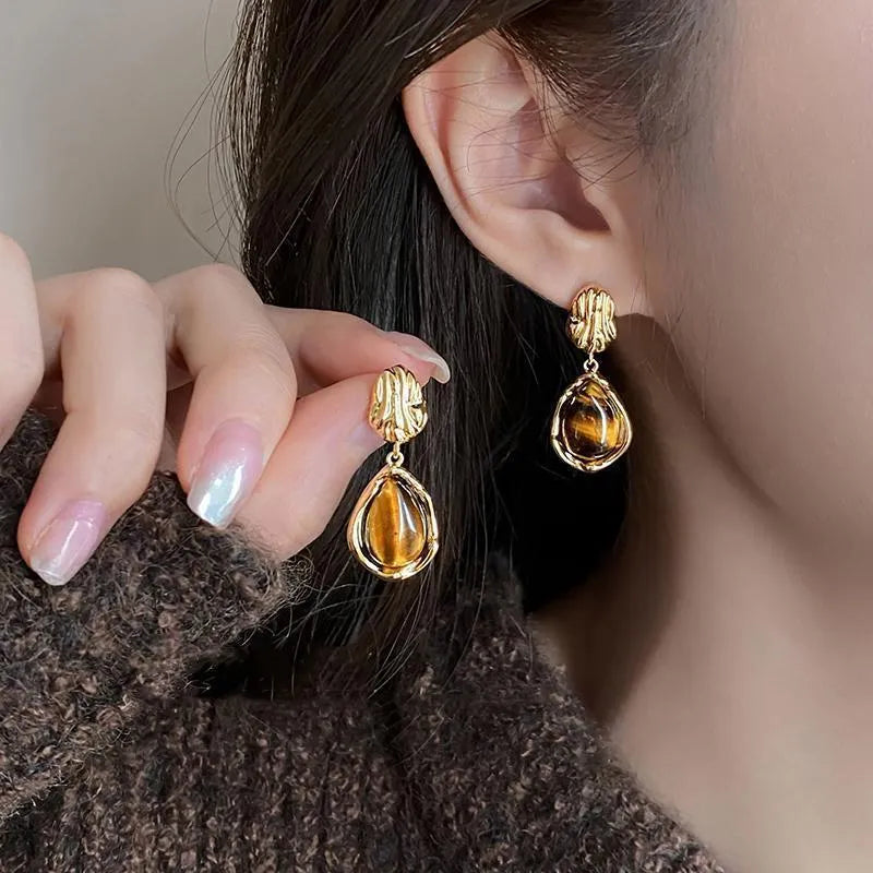 Handmade geometric alloy earring set showing three styles: round pieces, amber studs, and tigereye drops with tassels.