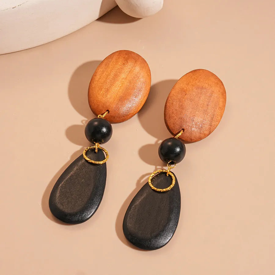 Pair of brown-black retro wooden ellipse earrings for women on a plain background.