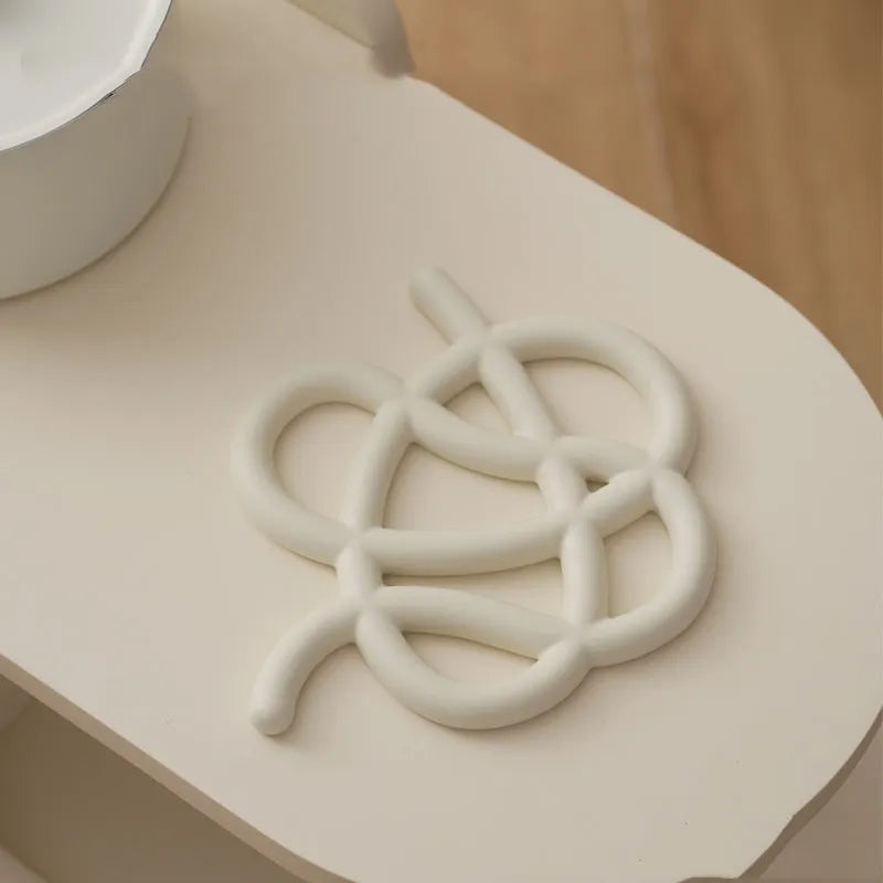 Modern irregular-shaped ceramic heat proof mat in grey on a wooden table protecting it from a hot pan.