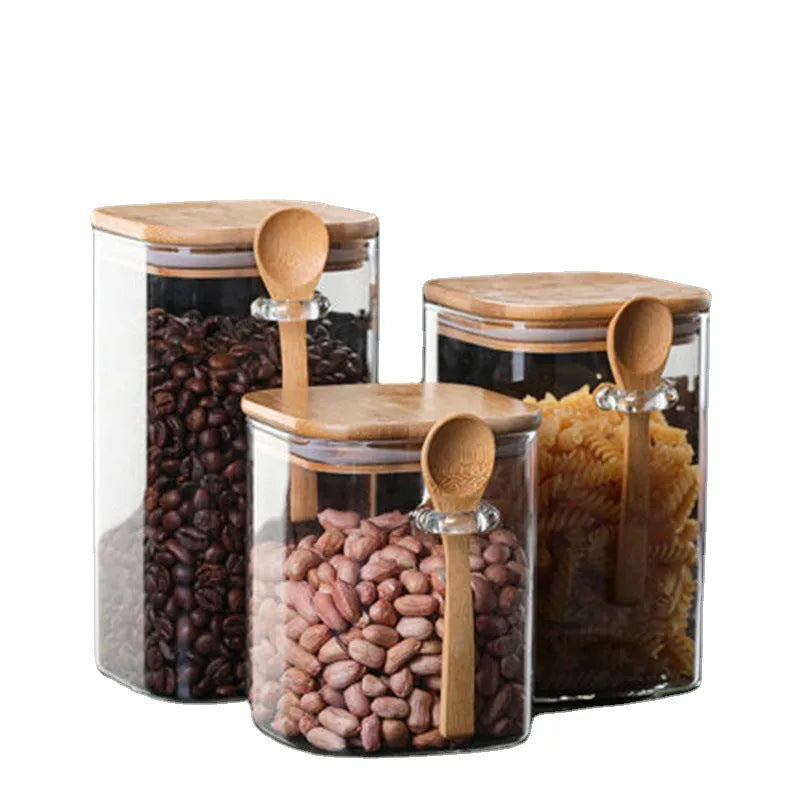 Square glass storage jar for coffee beans with wooden spoon on kitchen counter, clear body shows contents