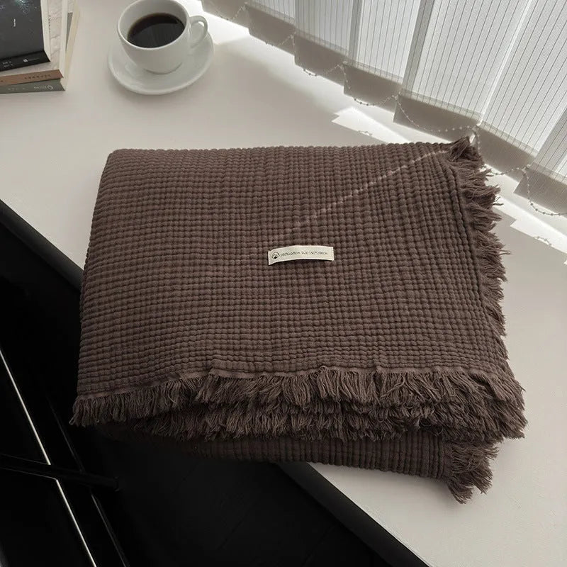 Cotton four-layer gauze blanket with tassel trim in avocado green colour, laid flat.