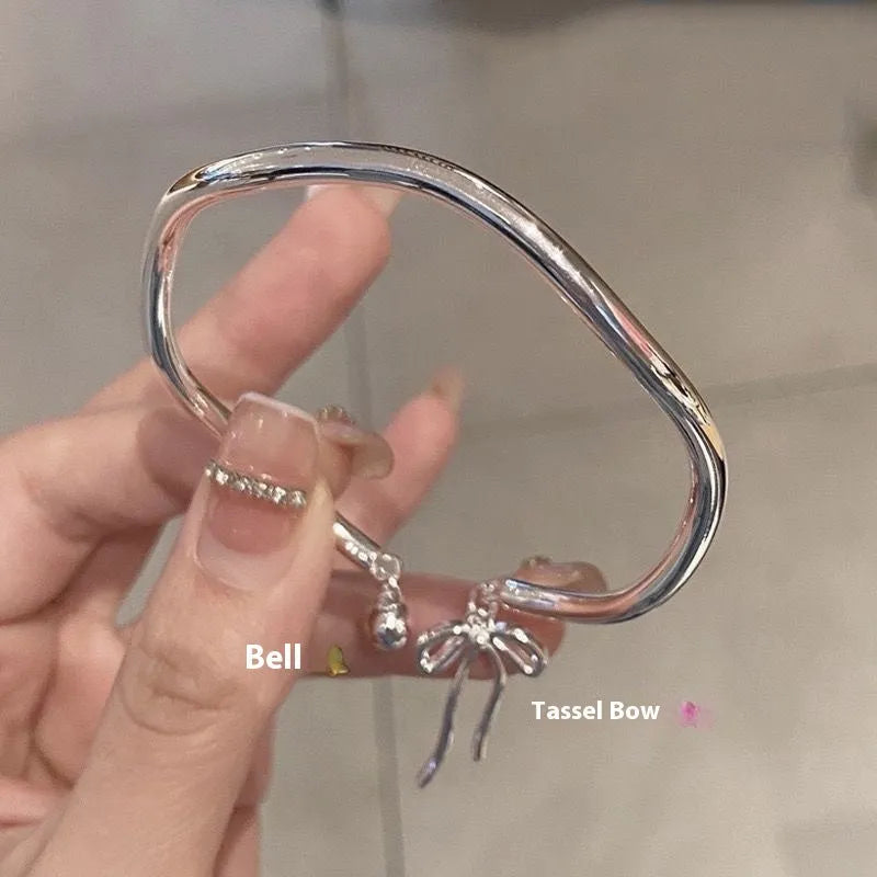 Silver adjustable bangle bracelet with a detailed bow charm and small bell on a wrist.