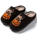 Pair of black plush house slippers with orange pumpkin print and a textured non-slip rubber sole.