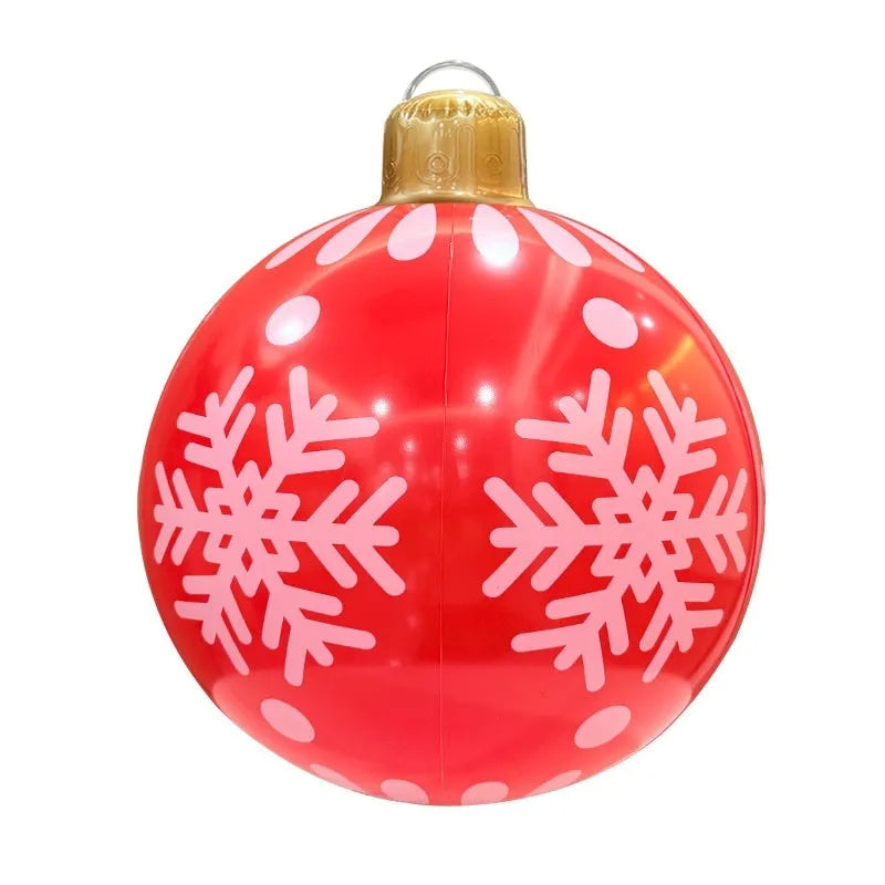 Large red inflatable Christmas ball with snowflake design and flashing lights in a garden setting.