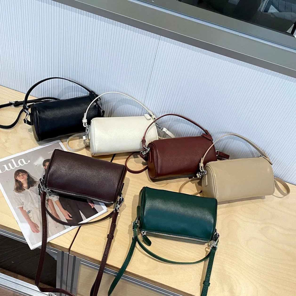 Cylindrical crossbody phone bag in soft genuine leather, shown in one of six colours including black or brown.