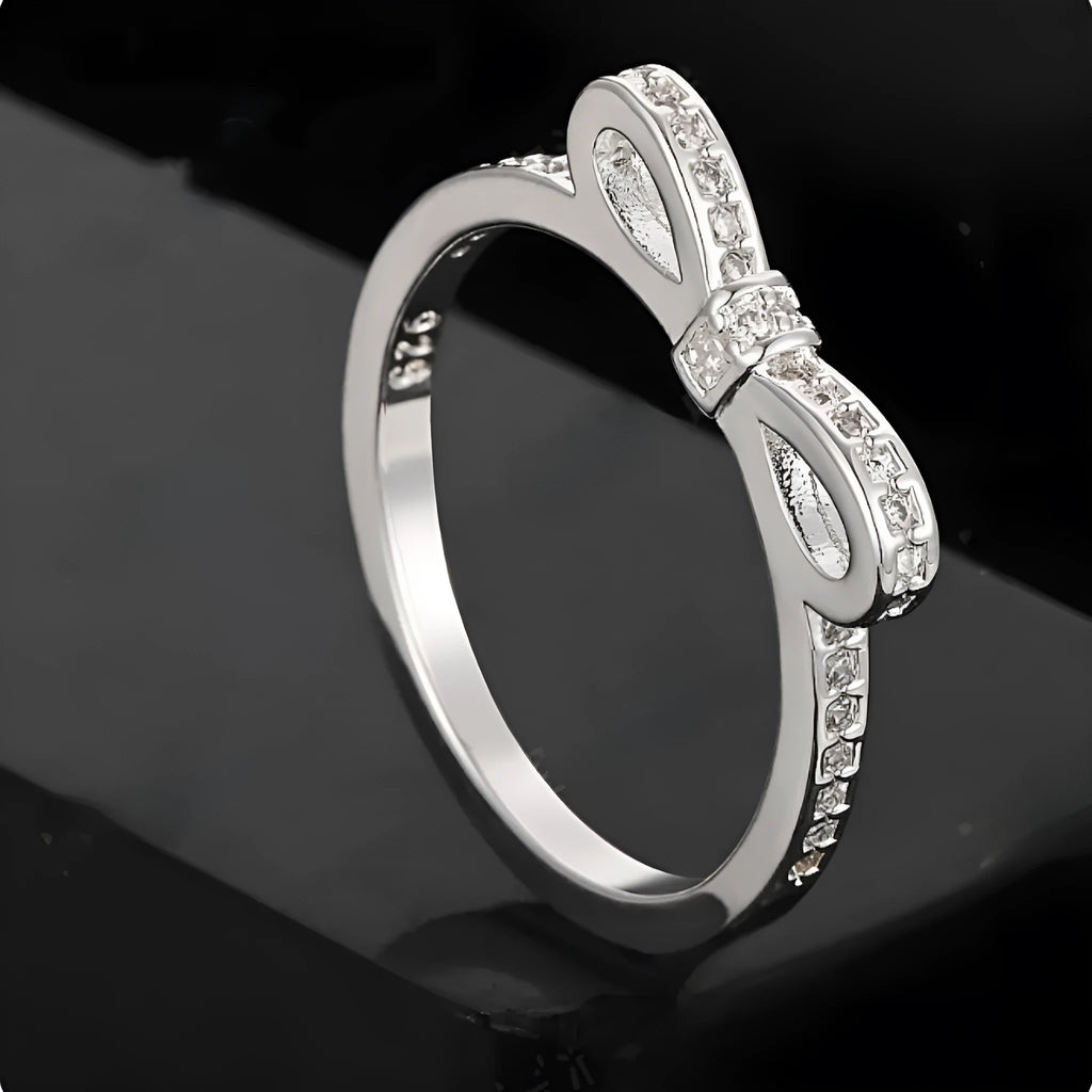 Silver coloured ring with a detailed three-dimensional bow design set with sparkling zircon crystals on a finger.