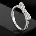 Silver coloured ring with a detailed three-dimensional bow design set with sparkling zircon crystals on a finger.