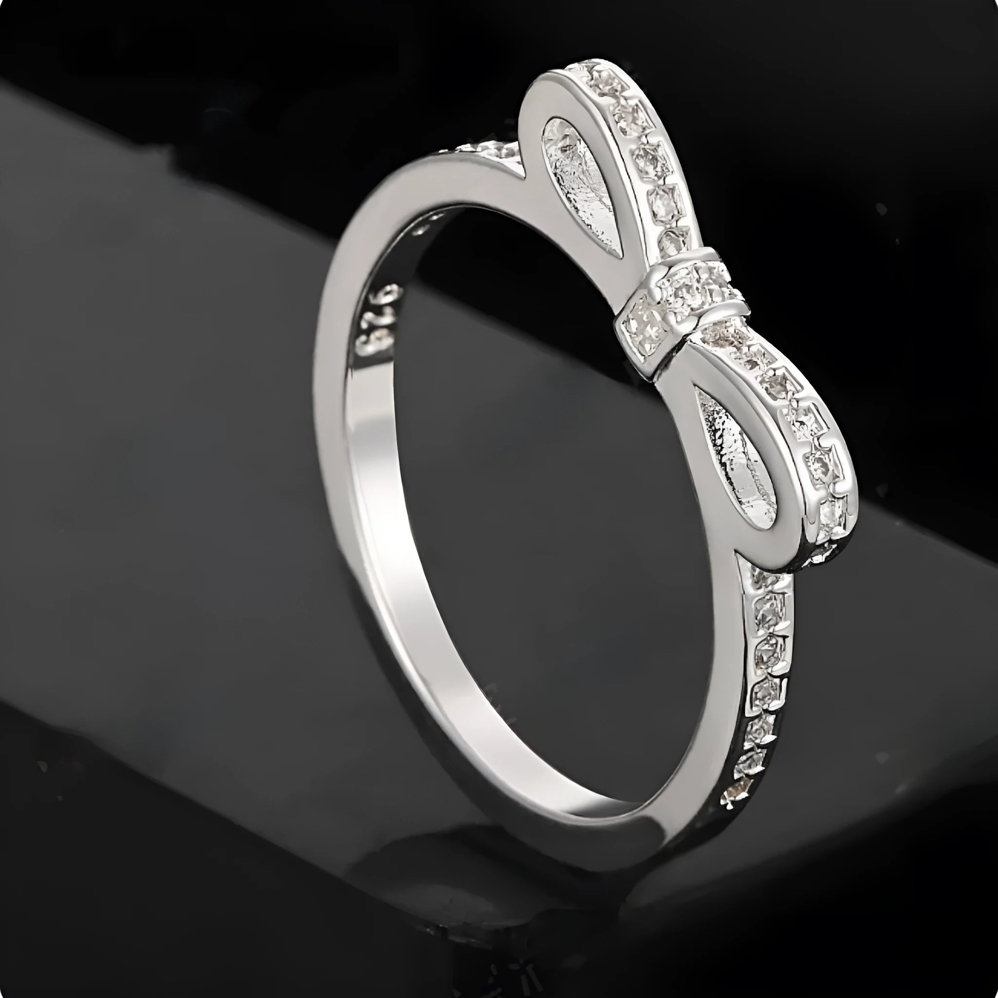Silver coloured ring with a detailed three-dimensional bow design set with sparkling zircon crystals on a finger.