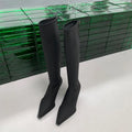 Women's black pointed toe below-knee boots with a stiletto heel and a back zipper on a plain background.