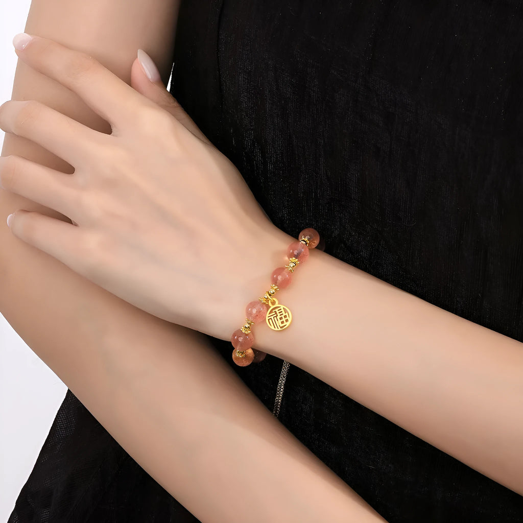 Women's strawberry quartz bracelet with geometric charms and fu character on wrist