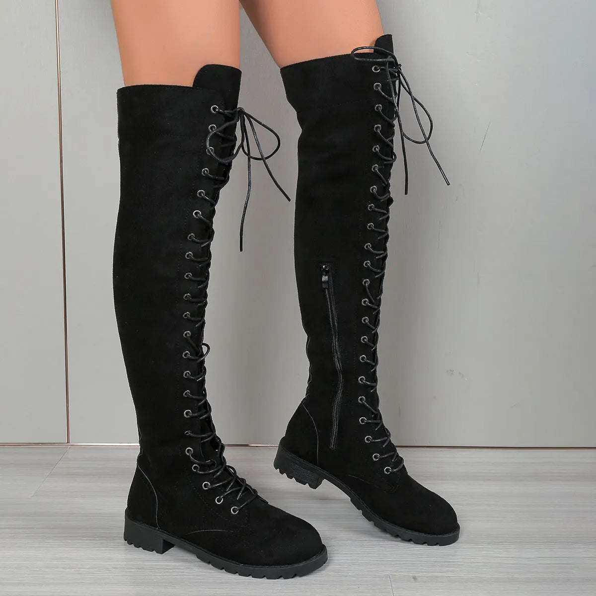 Black lace-up over-the-knee boots with round toe and flat rubber sole on a neutral background