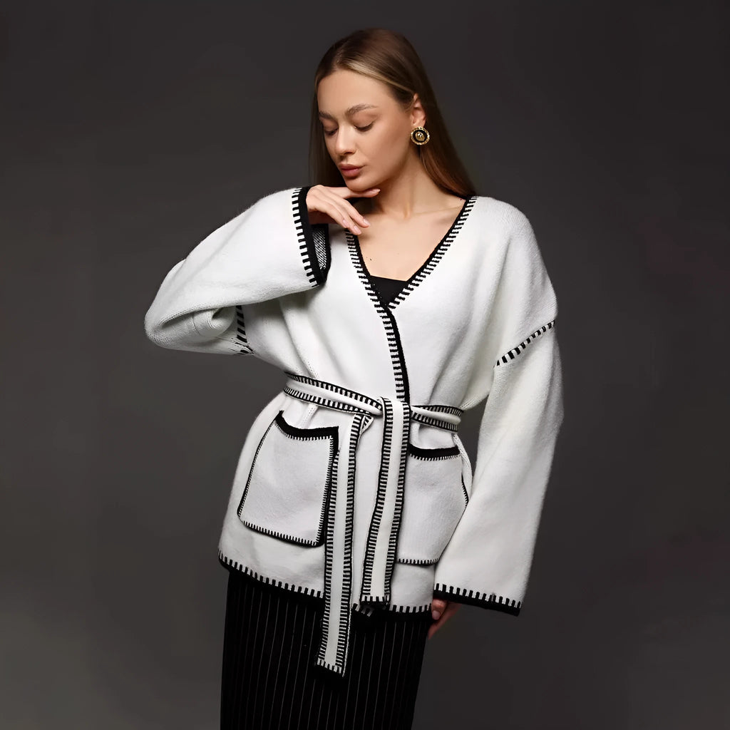 Loose beige knitted cardigan with a lace-up front, worn open over a white top.