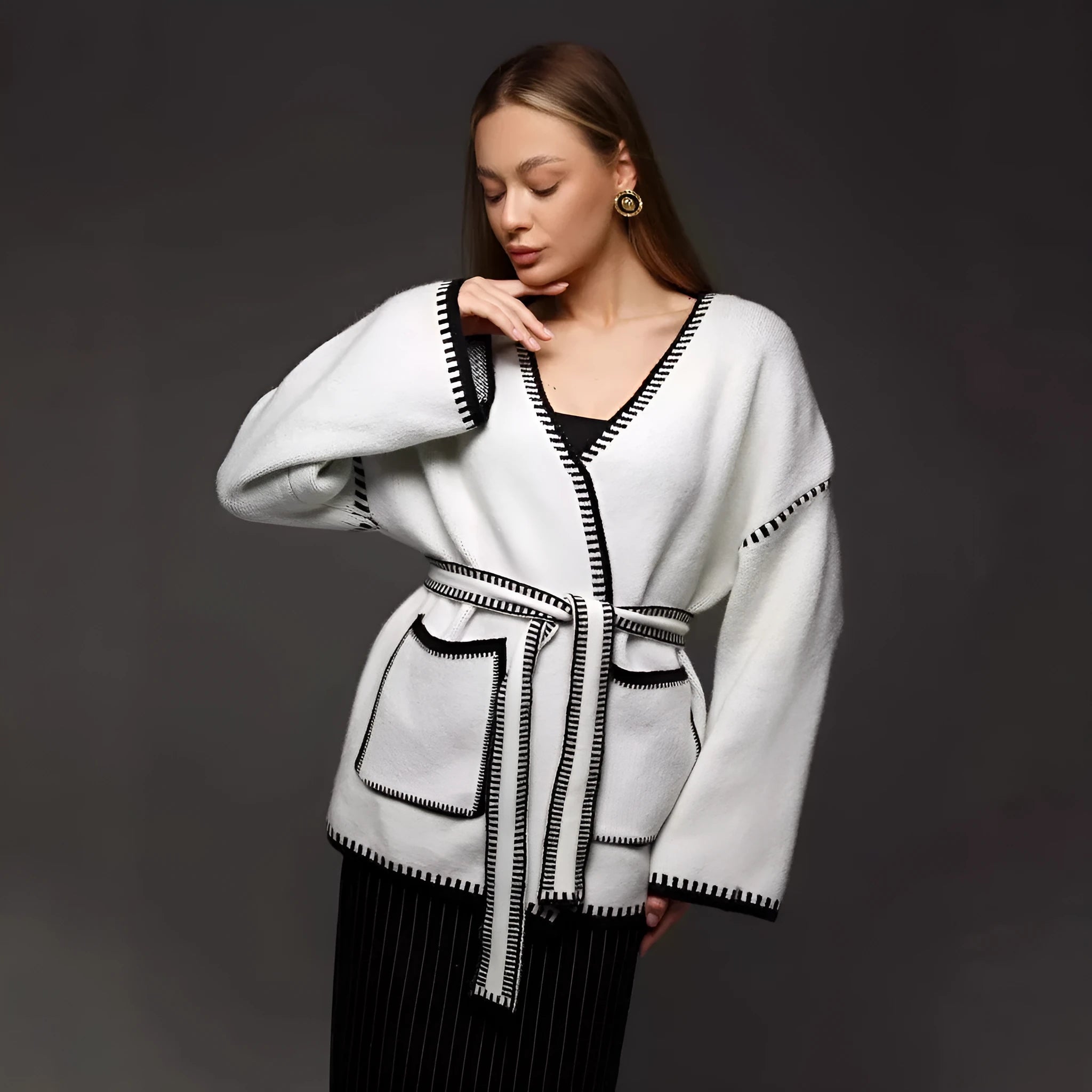 Loose beige knitted cardigan with a lace-up front, worn open over a white top.