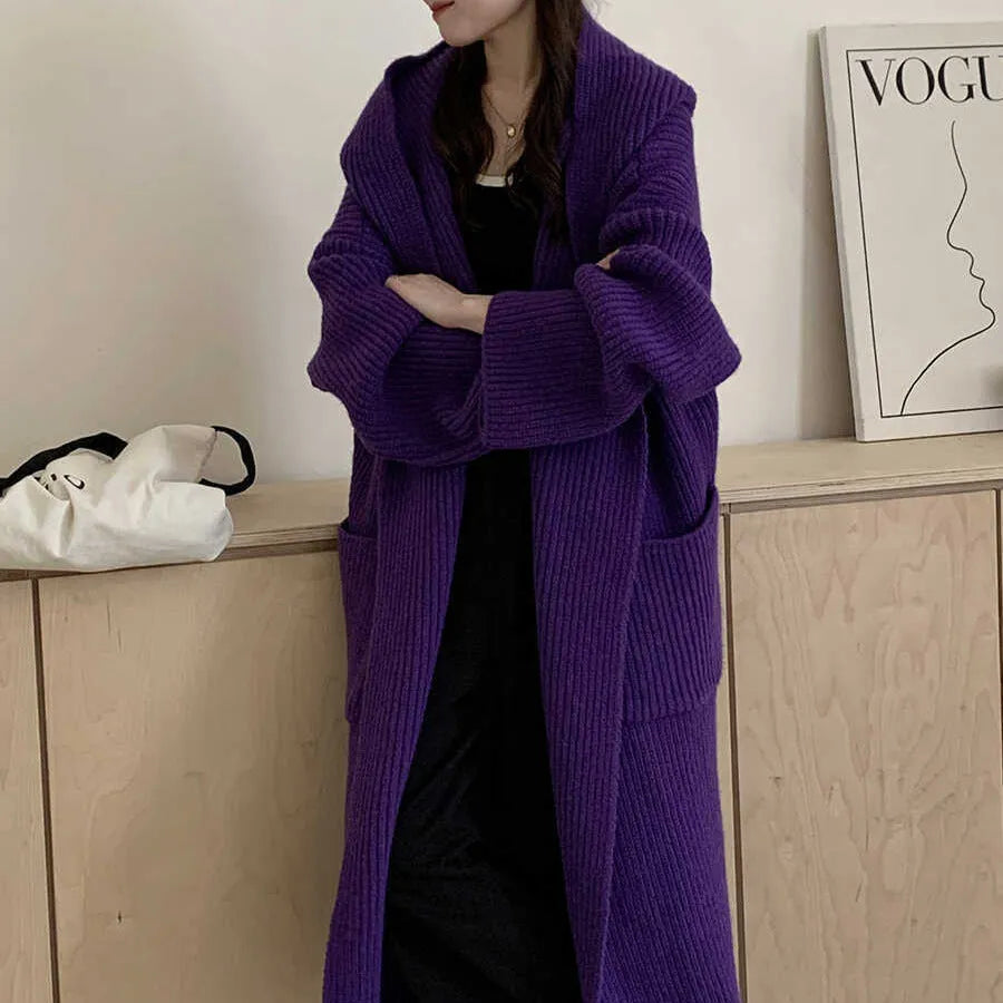 A woman wearing a long, loose, hooded cardigan coat in a neutral colour, showing its oversized fit and length.