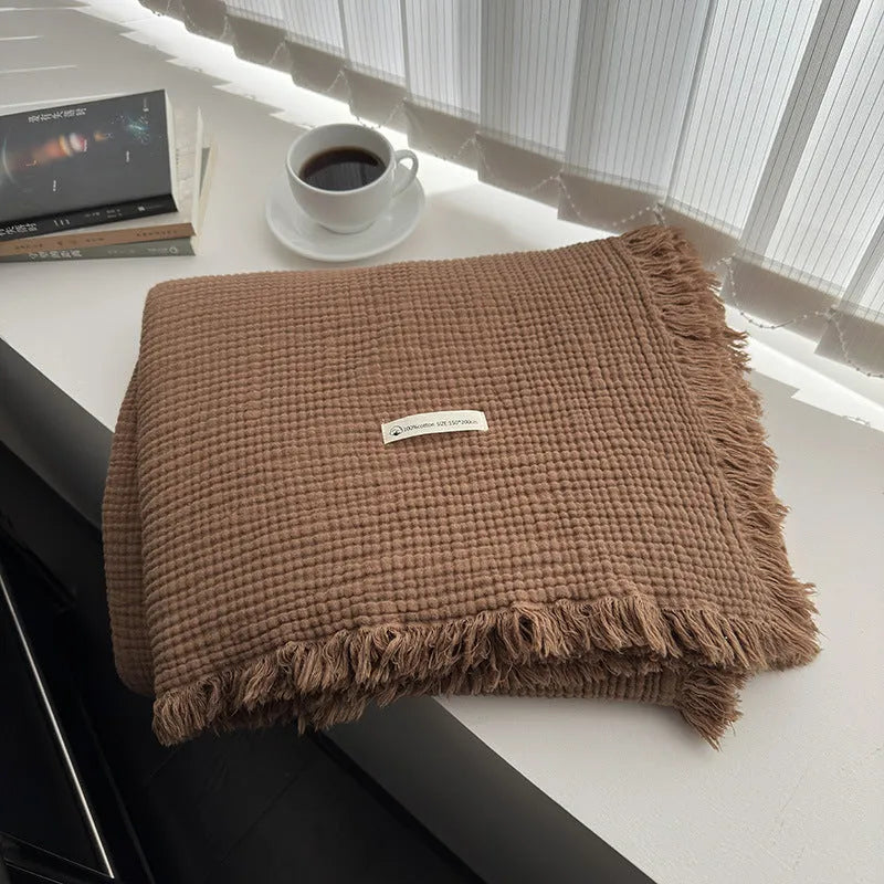 Cotton four-layer gauze blanket with tassel trim in avocado green colour, laid flat.