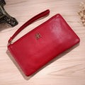 Long wine red crossbody handbag with a front zip phone pocket and an adjustable long strap on a table.