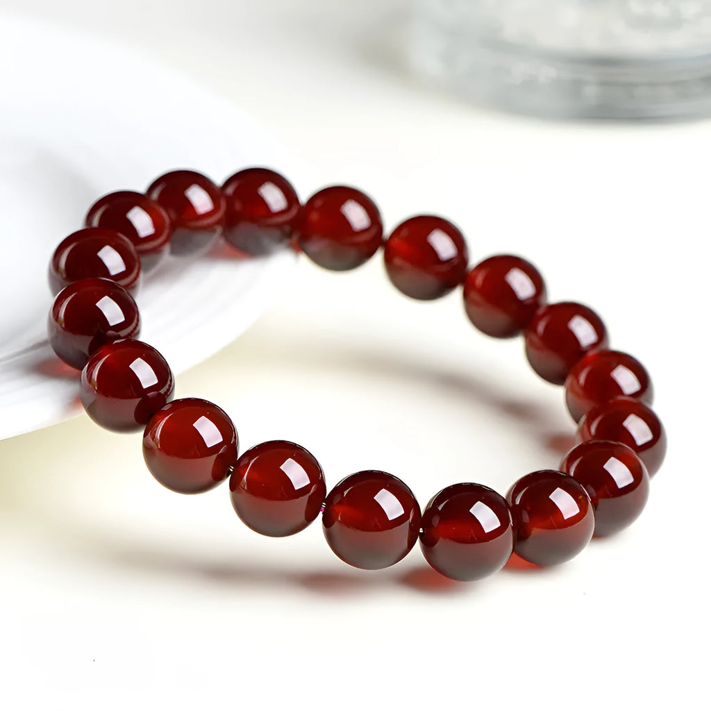 Close-up of a natural orange red garnet bead bracelet with a metal Ruyi charm on a wrist.