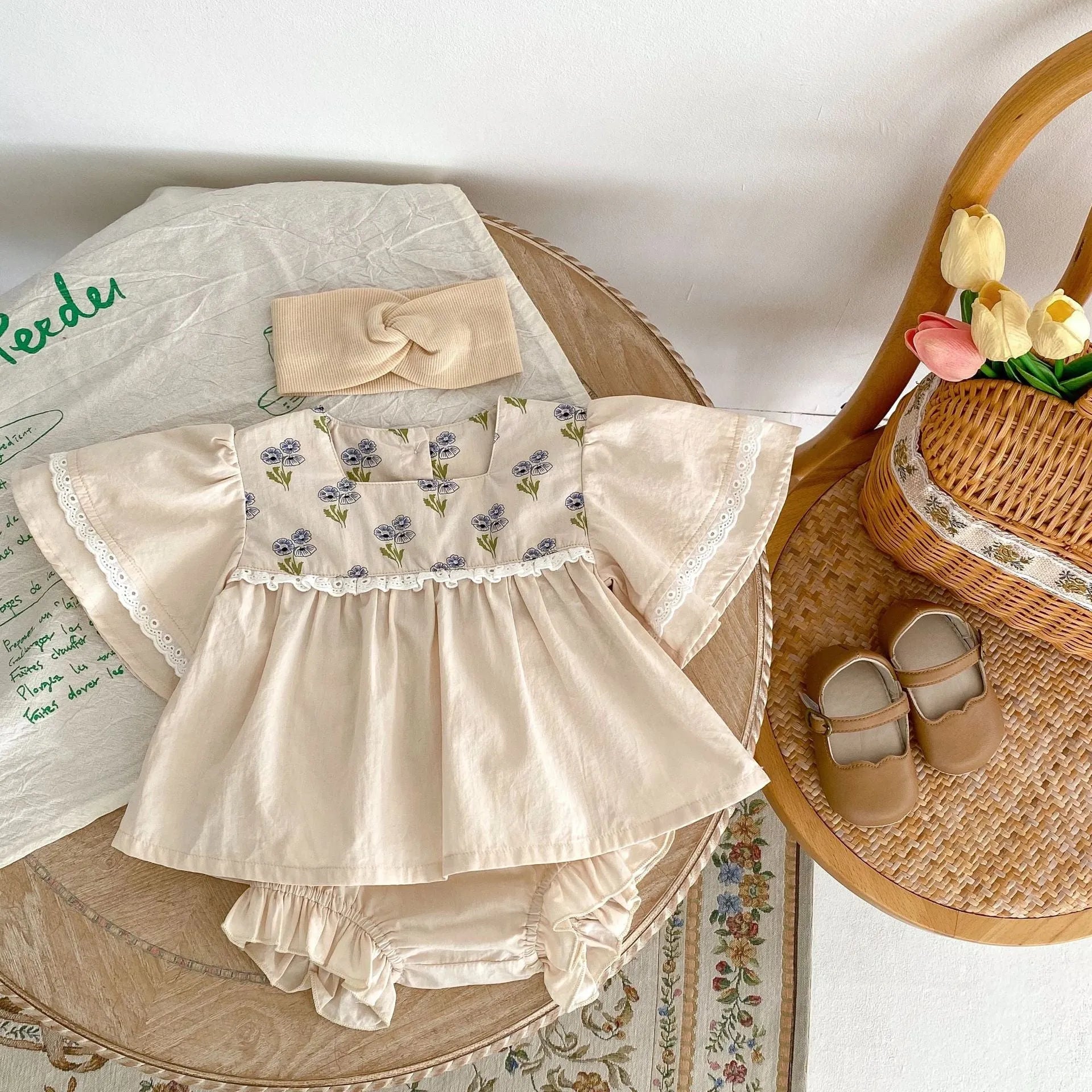 Apricot cotton two-piece suit with floral pattern, square collar top, and wooden horn buttons, next to matching bloomer pants.