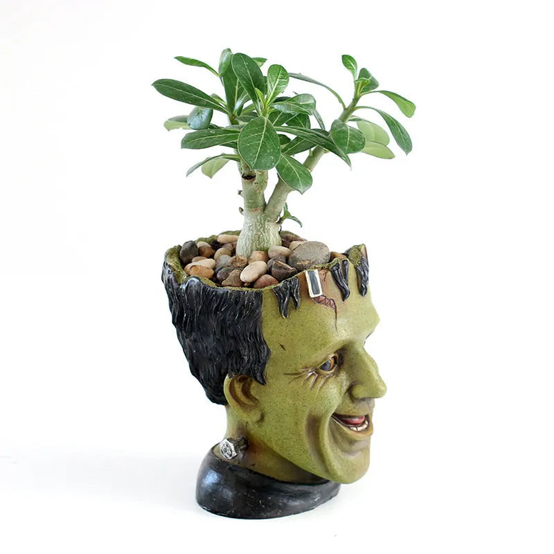 Green Frankenstein monster resin flower pot on a desk with a small succulent plant inside