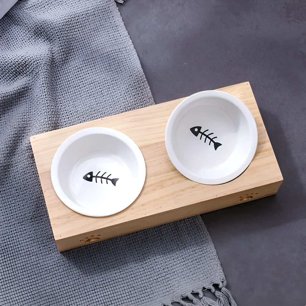Solid wood elevated pet feeder with stainless steel bowls in a bamboo finish on a wooden floor.