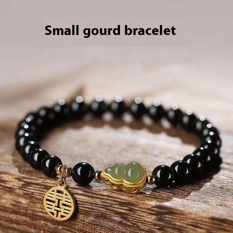 Black obsidian bracelet with a carved Hetian jade gourd charm, showing geometric beads.