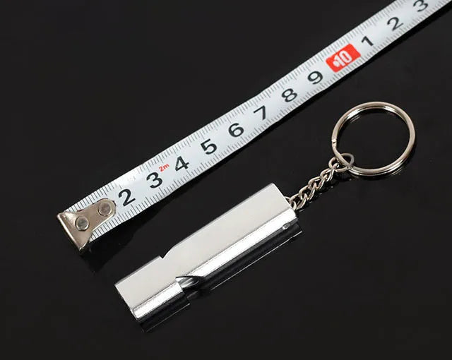 A silver or gold coloured aluminium alloy survival whistle with two holes on a grey background.